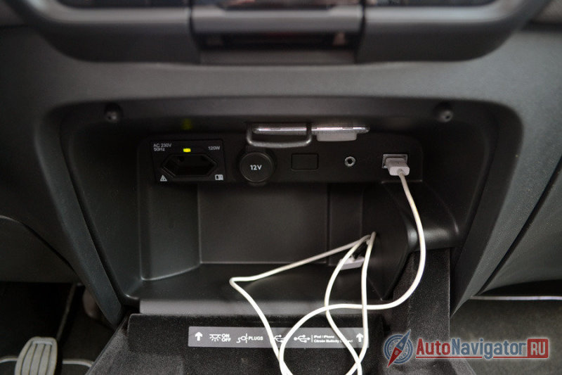 Во многом благодаря отсутствию лишних кнопок на центральной консоли, внизу удалось сделать дополнительный бардачок  для всяких гаджетов и телефонов. Примечательно, что тут же есть и розетка на 230V, розетка на 12V, usb и aux-разъемы.
А крышка этого бокса отделана мягкой тканью, так что ничего греметь не будет. Более того, можно ее не закрывать и поставить туда смартфон в качестве навигатора (там даже есть специальная выемка), переключать передачи это абсолютно не мешает