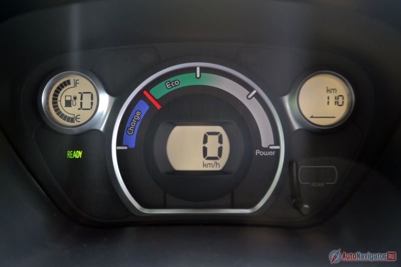 Скорость высвечивается в цифровом виде на центральном экране, слева расположен индикатор заряда, справа – бортовой компьютер, который на данной фотографии показывает запас хода. Основной стрелочный прибор – эконометр. Чем правее стрелка, тем больше энергии тратится, в синюю зону стрелка уходит только при рекуперативном торможении. Надпись «Ready» загорается, когда машина «заведена»